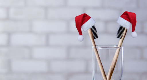 2 toothbrushes with santa hats sit in a glass cup