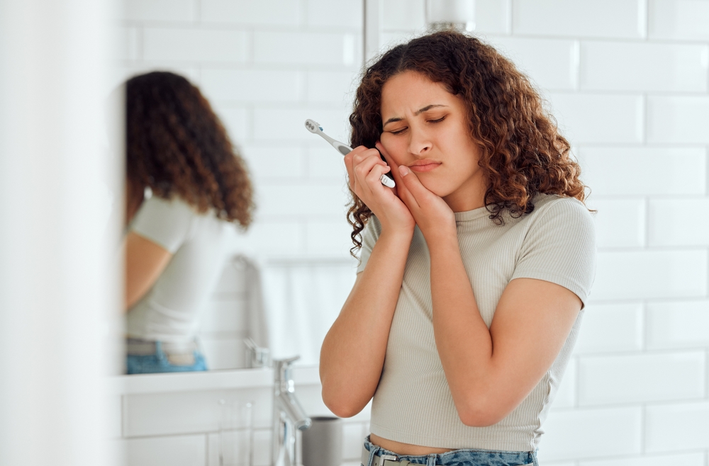 young woman holding her jaw after brushing her teeth because she lost a dental filling or crown